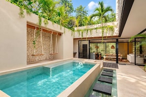 A modern outdoor pool area with a stone wall, hanging plants, and a seating area with a table and chairs. - Remodeled 4BR Boho Villa · Pool Trilogy + Hot Tub (Tulum)