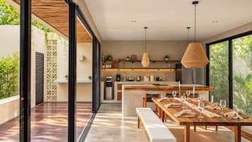 A modern kitchen with a central island, pendant lighting, and a dining area with a long table and benches.