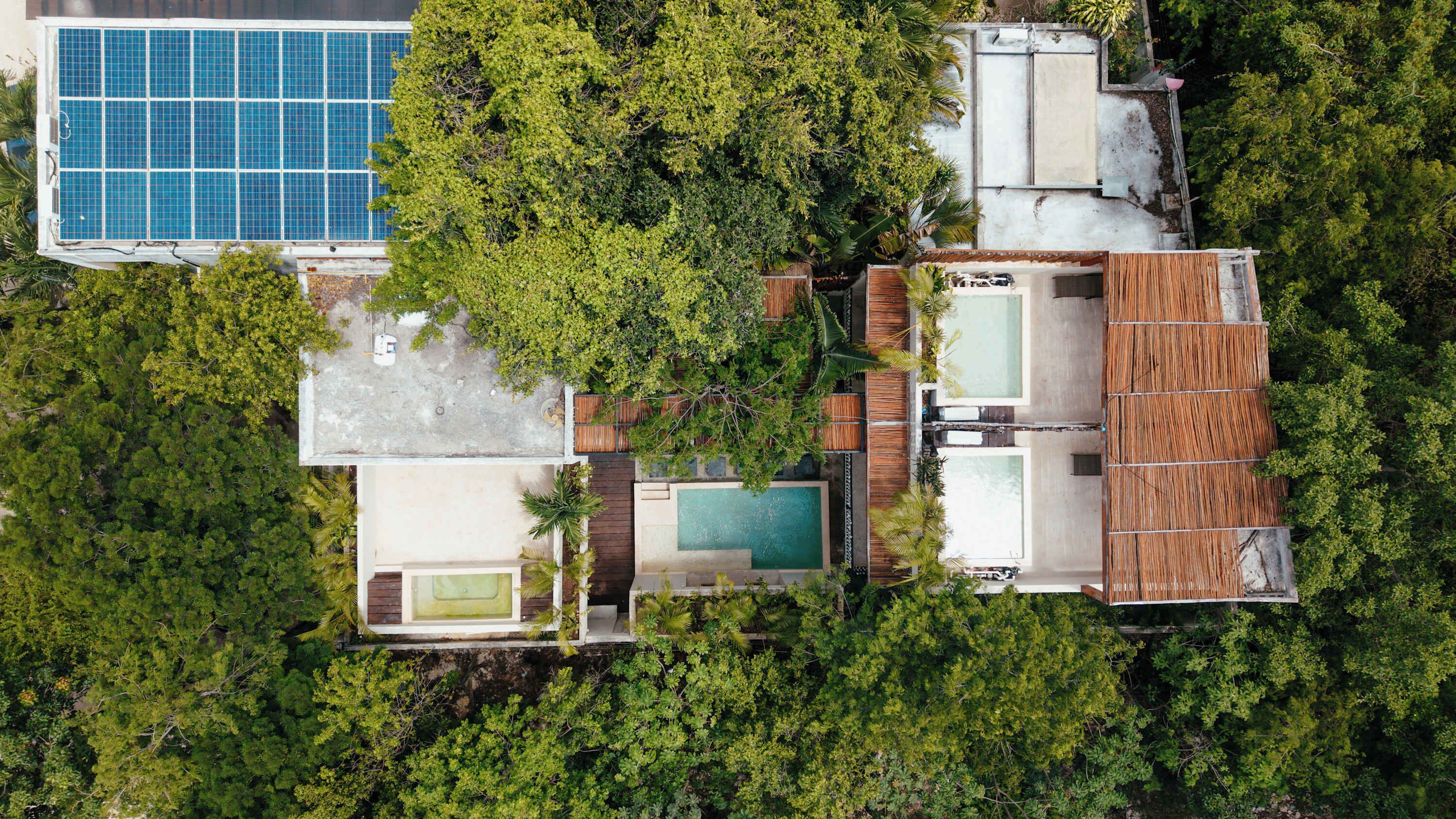 An aerial view of a resort with multiple swimming pools, a large blue solar panel, and lush greenery.