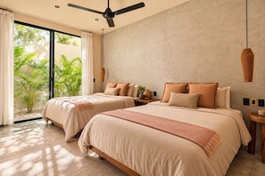 A hotel room with two beds, a ceiling fan, a large window with curtains, and a view of greenery outside. - Remodeled 4BR Boho Villa · Pool Trilogy + Hot Tub (Tulum)