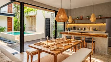 A modern kitchen with a central island, a dining area with a wooden table and benches, and a pool visible through large glass doors.
