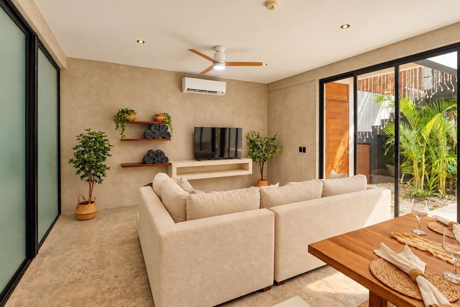 A modern living room with a sofa, TV, ceiling fan, and potted plants.