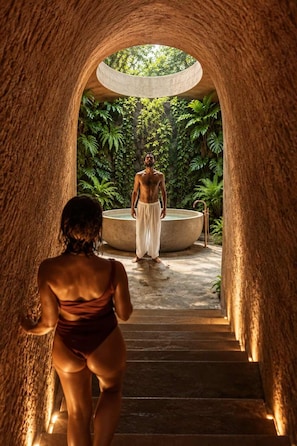 A man standing in a circular stone structure with a woman walking towards him through a tunnel-like passageway. - Penthouse| Private Pool| Hot & Cold Plunge + Spa (Tulum)
