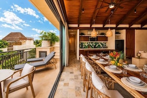 A dining area with a long table set for a meal, a balcony with lounge chairs, and a view of the surrounding landscape. - Penthouse| Private Pool| Hot & Cold Plunge + Spa (Tulum)
