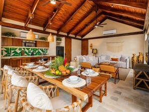 A spacious dining area with a long wooden table set for a meal, surrounded by wicker chairs. - Penthouse| Private Pool| Hot & Cold Plunge + Spa (Tulum)