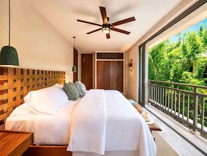 A bedroom with a bed, a ceiling fan, a nightstand, a window with a view of greenery, and a balcony railing. - Penthouse| Private Pool| Hot & Cold Plunge + Spa (Tulum)