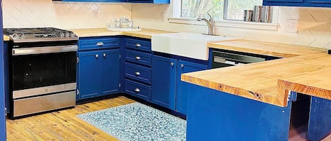 A kitchen with blue cabinets, a microwave, a stove, and a window with curtains.