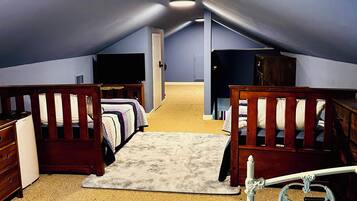 A room with a sloped ceiling, two beds with wooden headboards, a small white dresser, and a television on the wall.