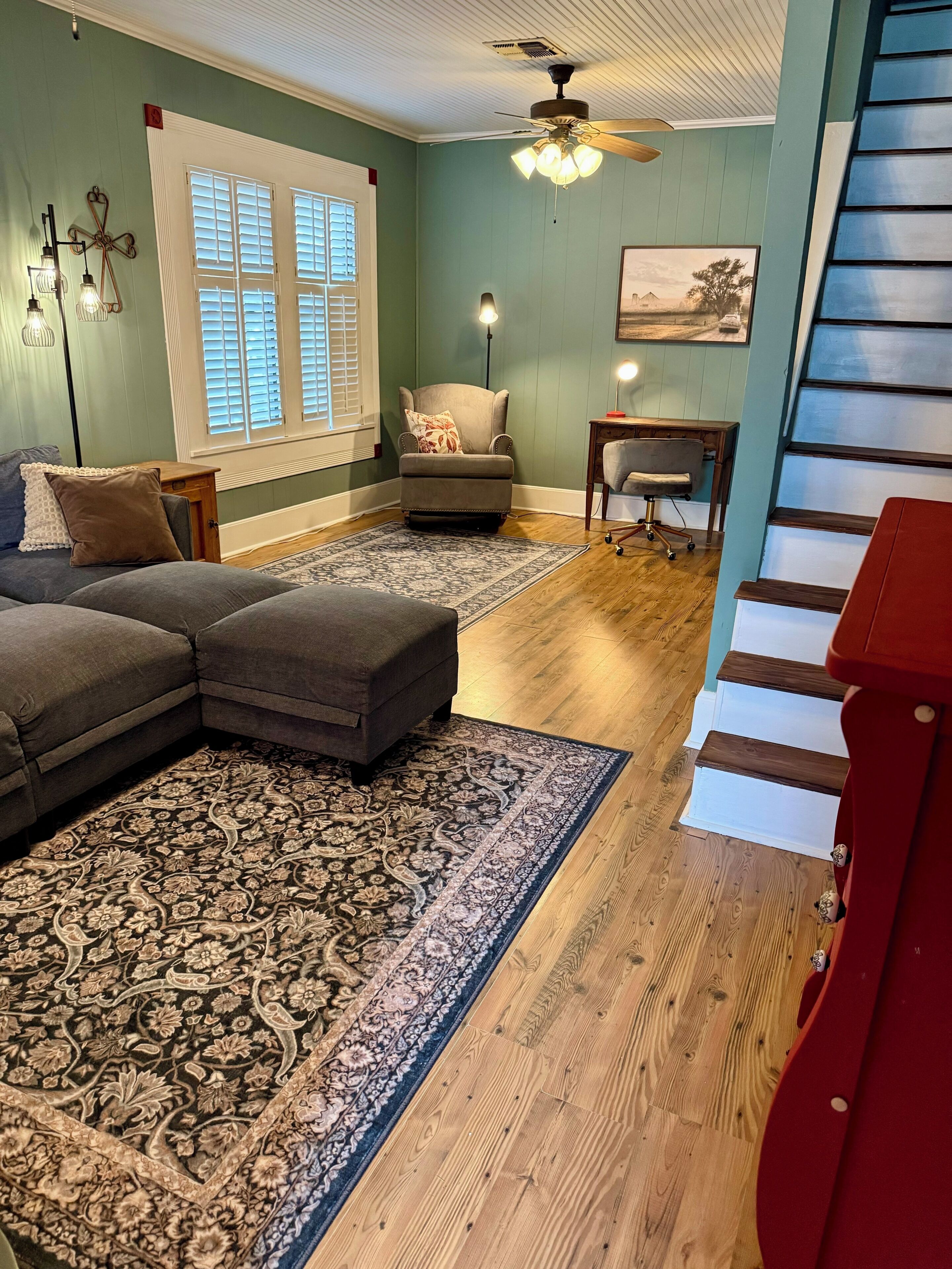 A living room with a sectional sofa, a patterned rug, a chair, a table, and a staircase.