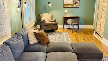 Una sala de estar con un sofá modular, un escritorio, una silla y un ventilador de techo.