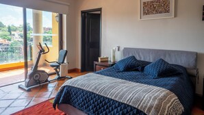 A bedroom with a bed, a chair, an exercise bike, and a door leading to a balcony. - Lujo y confort capilla SM de Allende (San Miguel de Allende)