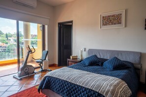 Un dormitorio con cama, una silla, una bicicleta estática y una puerta que da a un balcón.