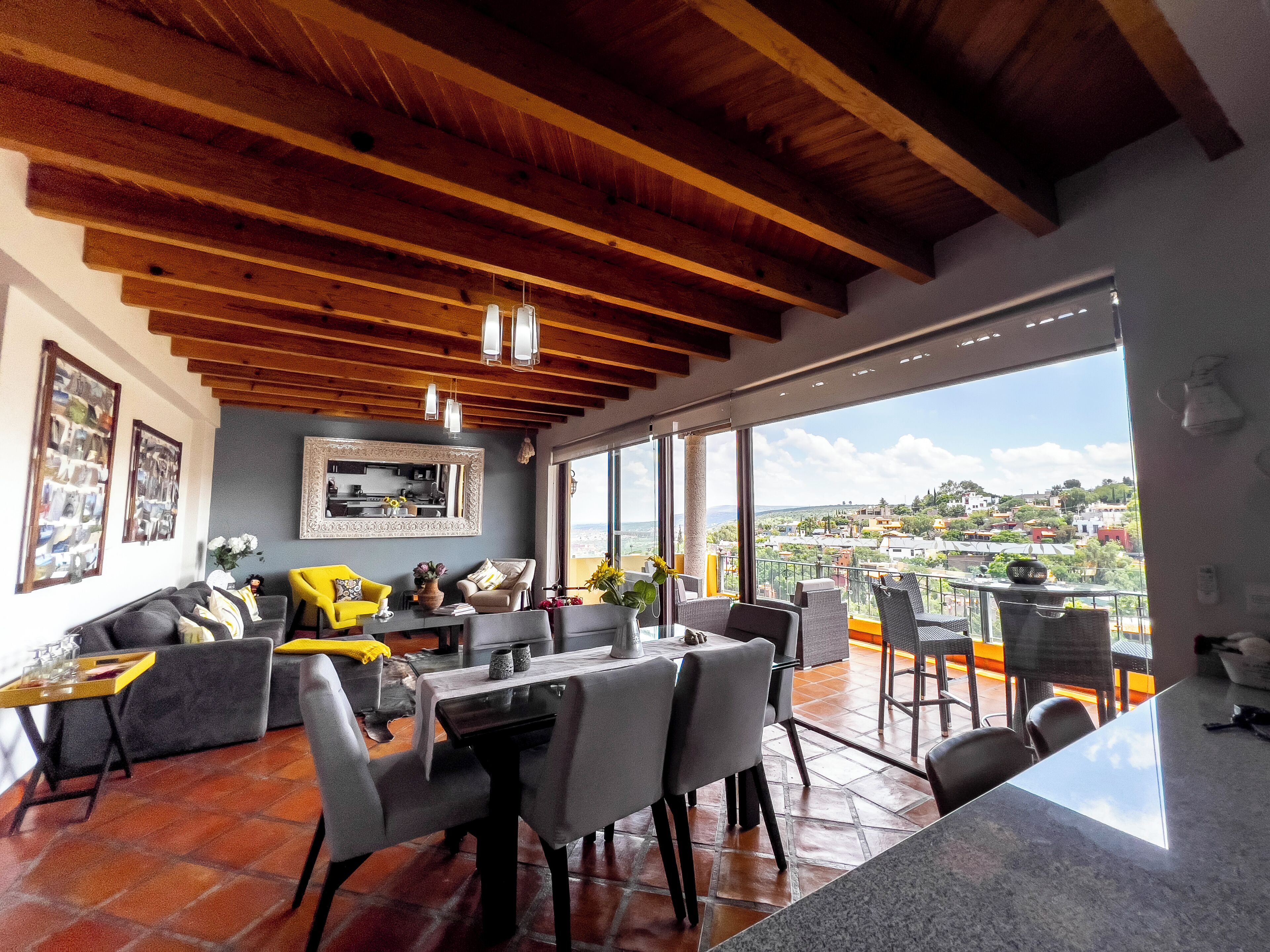 A dining area with a high ceiling, wooden beams, and a view of a cityscape through large windows.