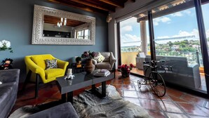 A modern living room with a large mirror, a yellow armchair, a sofa, a coffee table, and a view of a cityscape through large windows. - Lujo y confort capilla SM de Allende (San Miguel de Allende)
