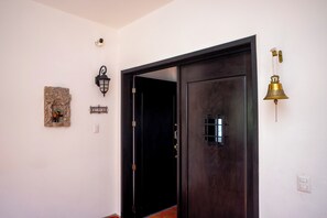 A hallway with a dark wooden door, a wall-mounted light fixture, a decorative stone piece, and a brass bell. - Lujo y confort capilla SM de Allende (San Miguel de Allende)