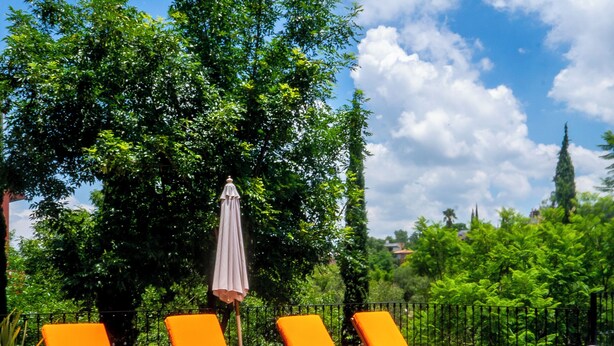 A swimming pool with blue mosaic tiles, surrounded by orange lounge chairs and a single umbrella. - Lujo y confort capilla SM de Allende (San Miguel de Allende)