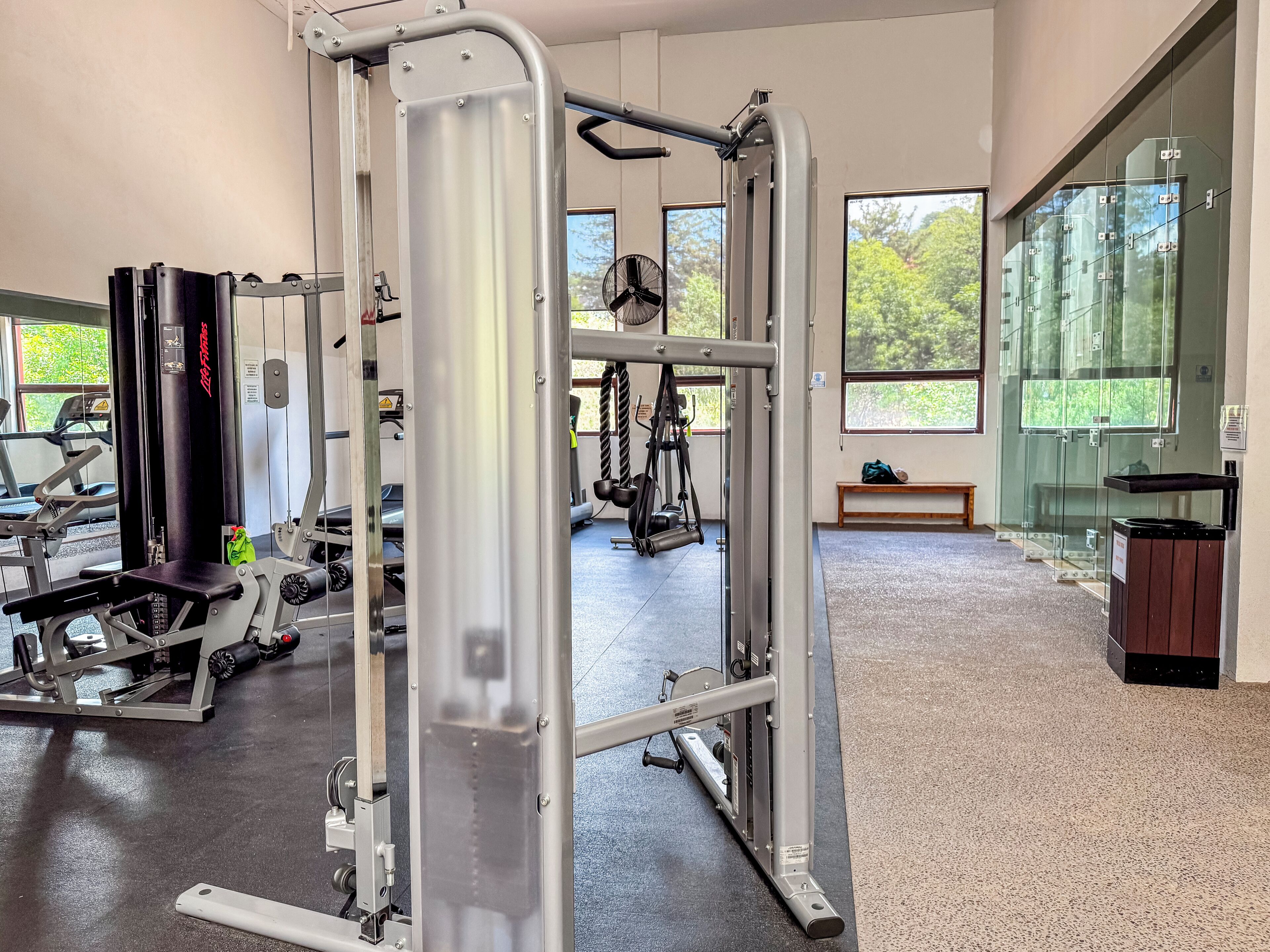 Une salle de sport équipée de divers appareils d’exercice, dotée de grandes fenêtres et d’un banc.