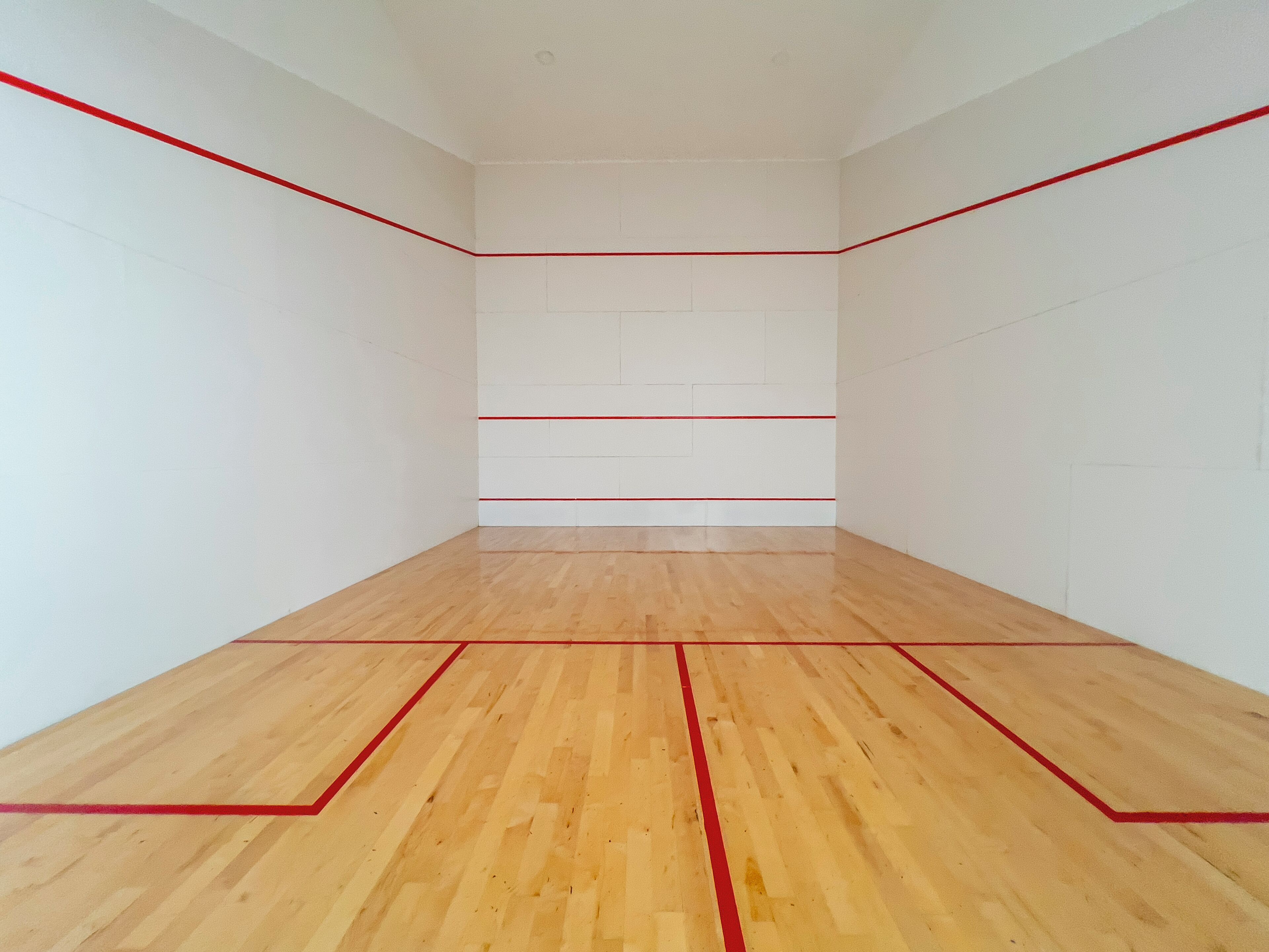 Una cancha de squash con piso de madera y líneas divisorias rojas.