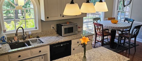 A kitchen with white cabinetry, a granite countertop, a built-in microwave, and a dining area with a table and chairs.
