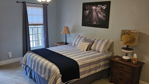 A bedroom with a bed, a nightstand, a lamp, a ceiling fan, and a window with curtains. - 3-bedroom house in Durham near UNC, Duke and the American Tobacco Trail (Durham)