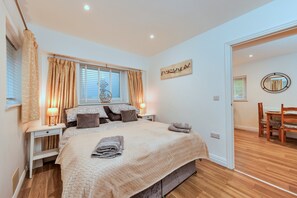 A bedroom with a bed, bedside tables, a window with curtains, a wall-mounted artwork, and a wooden floor. - Cosy Annexe by Hadrian's Wall (Brampton)