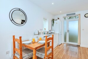 A modern kitchen with a dining table set for two, a round mirror, and a clock on the wall. - Cosy Annexe by Hadrian's Wall (Brampton)