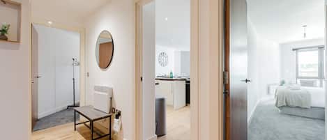 Un intérieur moderne avec un plancher en bois, un miroir, un radiateur et un coin cuisine visible à travers une porte ouverte.