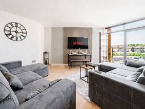 Ein modernes Wohnzimmer mit grauen Sofas, einem Flachbildfernseher und einem großen Fenster mit Blick auf die Stadt.