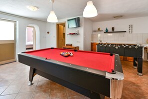 A pool table with balls, a foosball table, a television, and a kitchen area with a tiled backsplash. - Villa Ferlini with large private yard (Svetvinčenat)