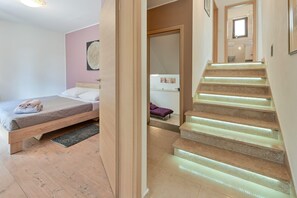 Ein Schlafzimmer mit einem Bett, einem Nachttisch, einem Fenster und einer Treppe mit beleuchteten Stufen.