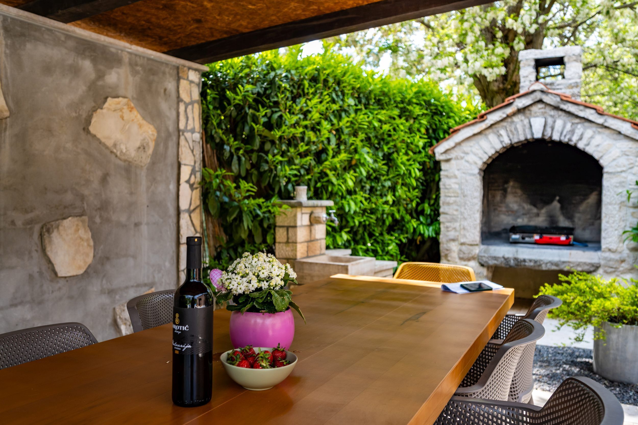 Une table en bois, une bouteille de vin, un bol de fraises et un vase rose orné de fleurs.