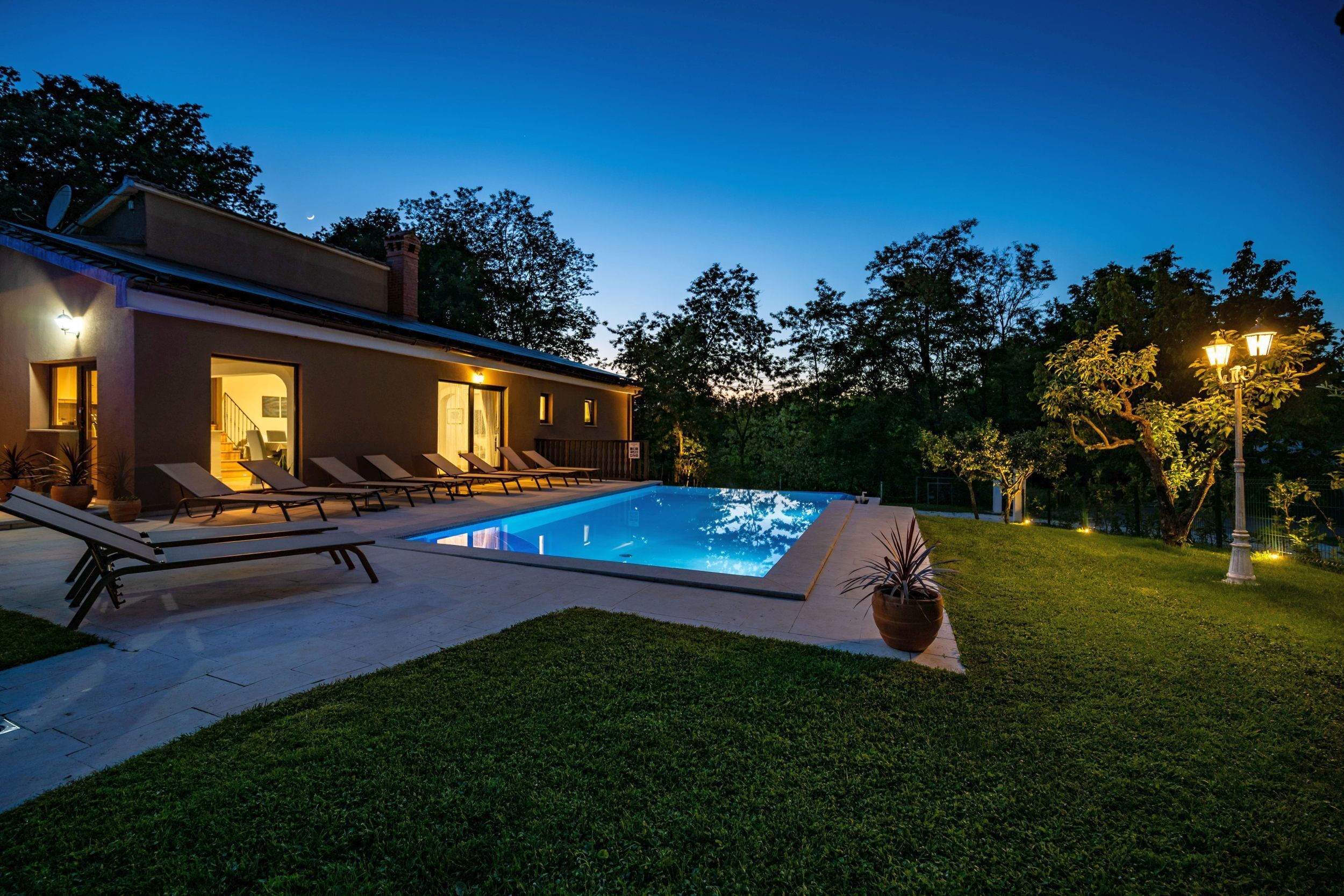 Ein modernes Haus mit Swimmingpool, Sitzgelegenheiten im Freien und einem gepflegten Rasen.