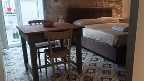 Une petite pièce avec un lit, une table et une chaise. Il y a une fenêtre donnant sur un balcon.