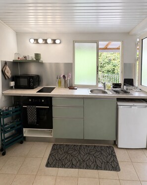 A compact kitchen with a microwave, oven, sink, and dishwasher. There is a window with a view of greenery outside. - L'Escapade Ludique | 80 Board Games & Private Terrace (Saint-Esprit)