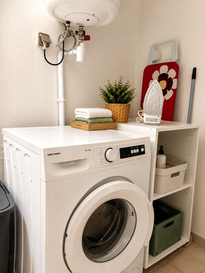 A Waltham washing machine in a laundry area with a sink, a plant, and a red flower-patterned board. - L'Escapade Ludique | 80 Board Games & Private Terrace (Saint-Esprit)