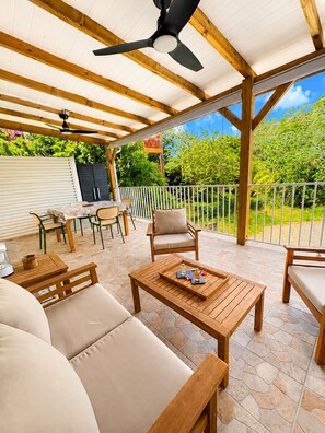 An outdoor patio with wooden furniture, a ceiling fan, and a view of greenery. - L'Escapade Ludique | 80 Board Games & Private Terrace (Saint-Esprit)