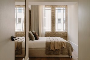 Ein Schlafzimmer mit einem Bett, einem Fenster mit Vorhängen und einer Ziegelwand.