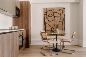A modern kitchen with wooden cabinetry, a built-in oven, and a dining area with a round table and four chairs. - Fulham Residences Four (London)