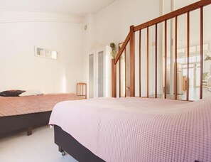Une chambre avec deux lits, un escalier en bois et une grande fenêtre.