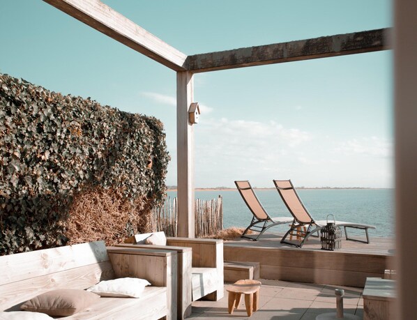 Une terrasse en bois avec un muret en pierre, deux chaises longues et une petite table.