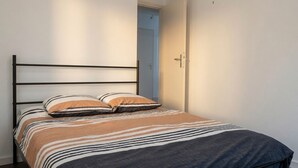 Un lit simple avec un cadre en métal, une couvre-lit à rayures et deux oreillers.