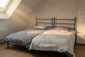 A bedroom with a bed, two pillows, a nightstand, a radiator, and a window with a triangular view. - Charming house just 5 minutes from the beach (Larmor-Plage)