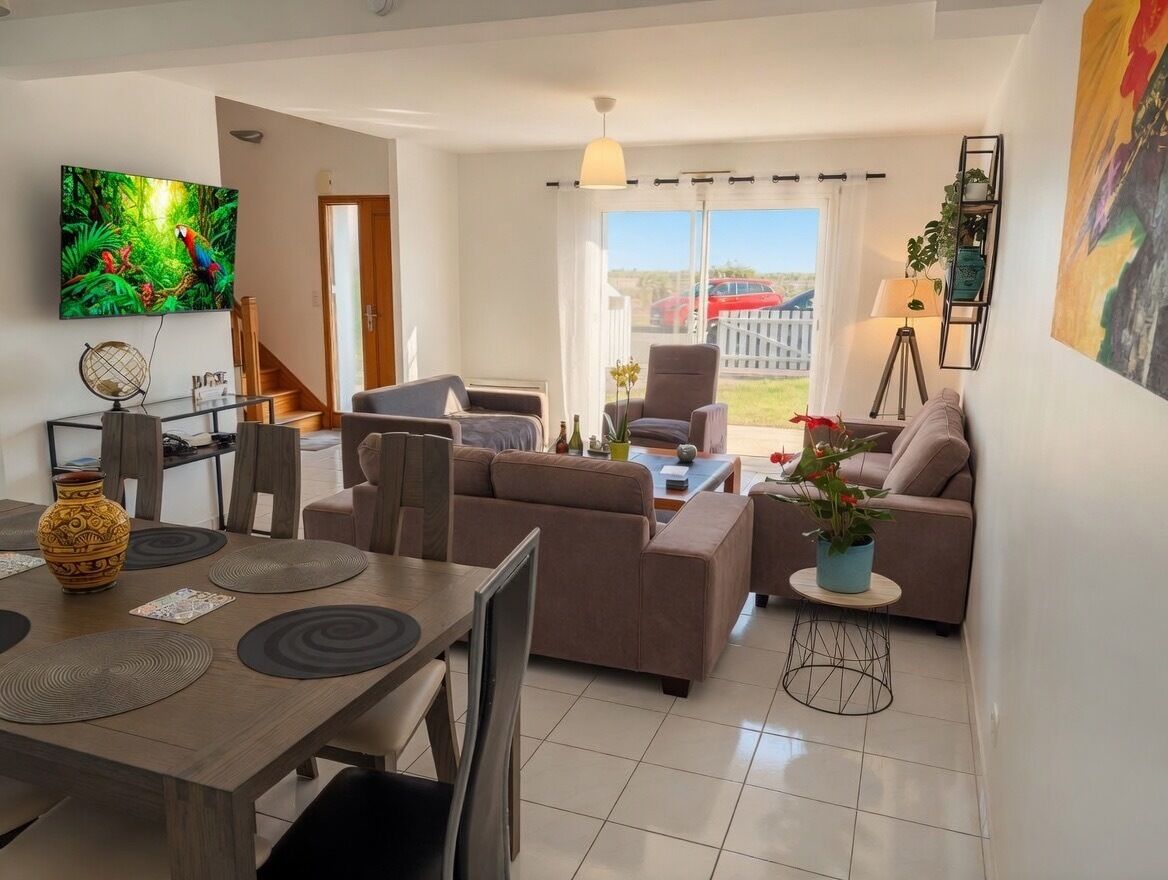 Una sala de estar moderna con un sofá, sillones, una mesa de comedor con individuales, un televisor montado en la pared y un balcón con vistas.