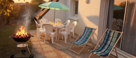 Un patio con una parrilla, sillas exteriores y una mesa con sombrilla.
