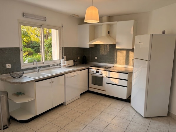 A modern kitchen with a built-in oven, a sink, and a refrigerator. - Charming house just 5 minutes from the beach (Larmor-Plage)