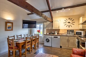 Un comedor con una mesa y sillas de madera, una cocina con electrodomésticos y un reloj de pared.