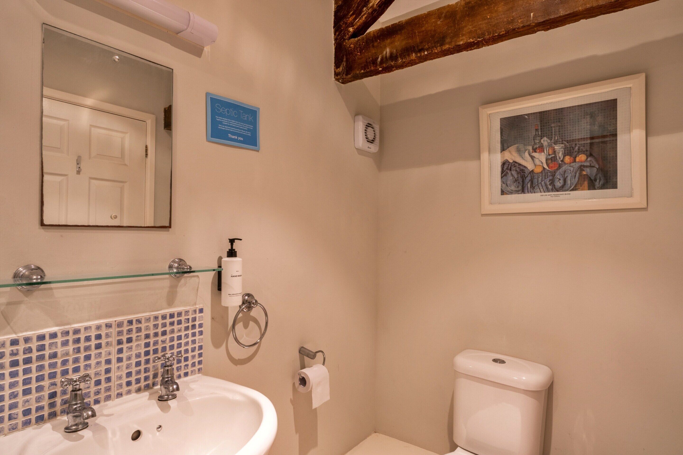 Un bagno con lavandino, specchio, servizi igienici e un'opera d'arte appesa al muro.