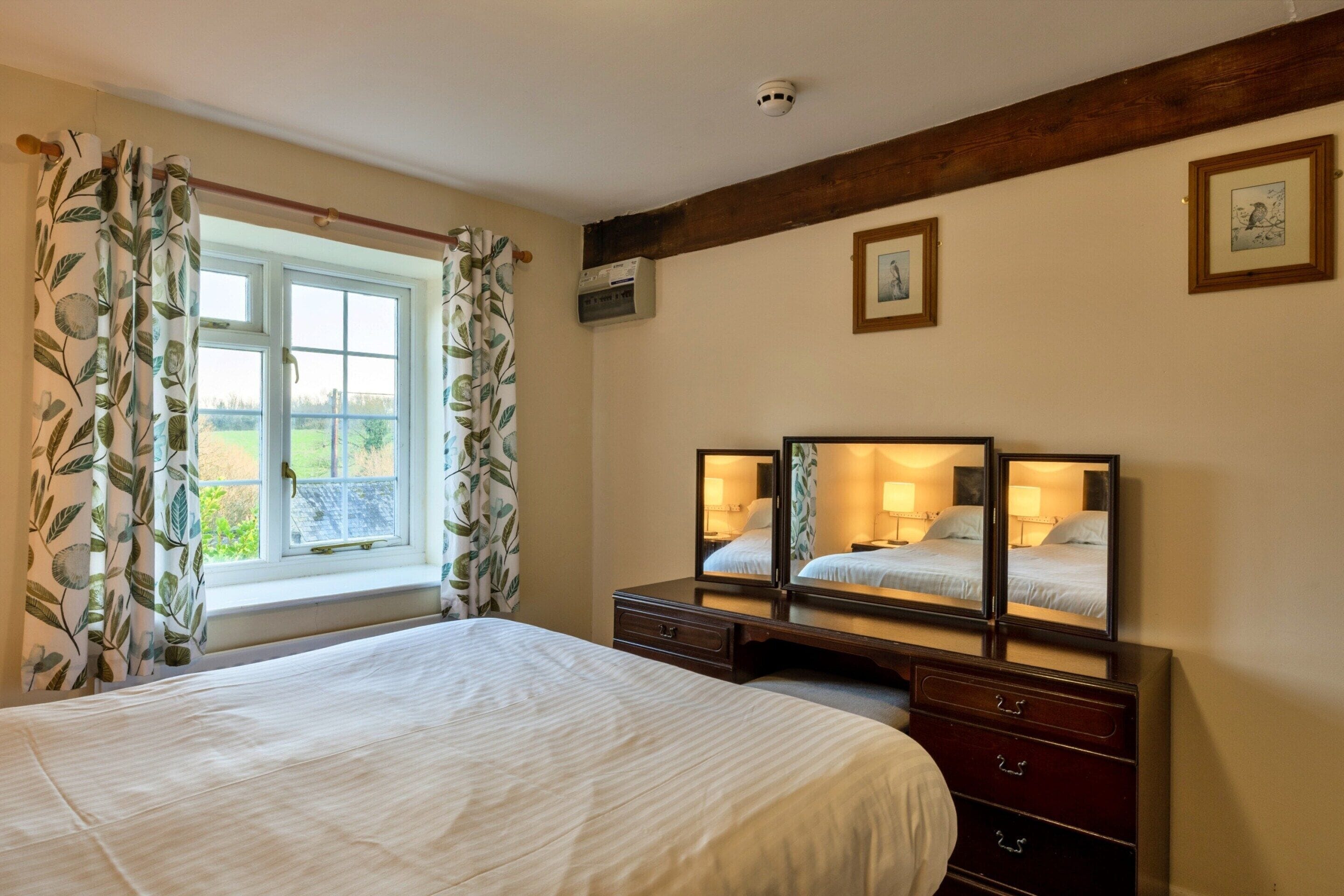 A hotel room with a large bed, a dresser with mirrors, and a window with curtains.