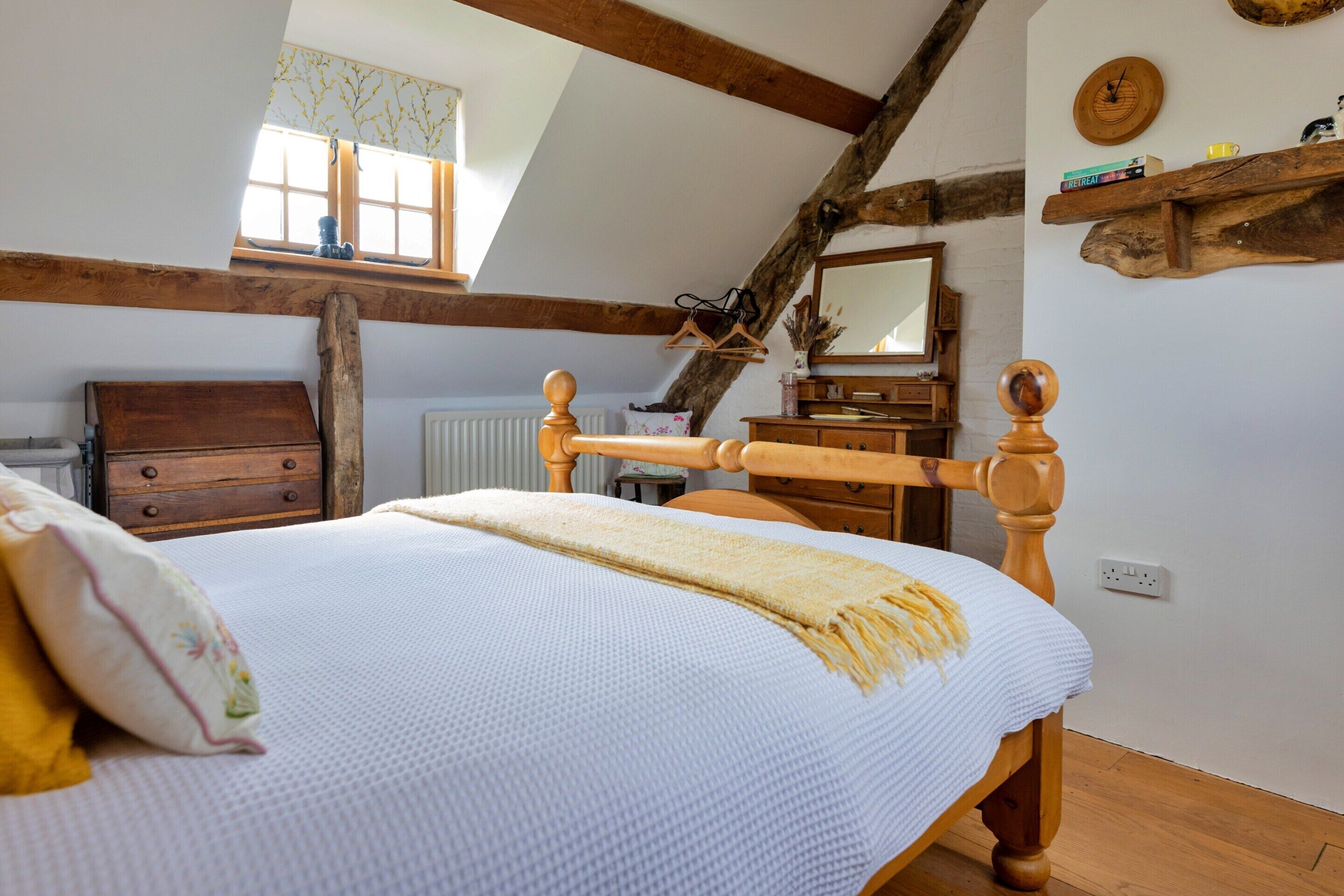 Une chambre à coucher avec un lit en bois, une commode, un miroir et une fenêtre avec des rideaux.