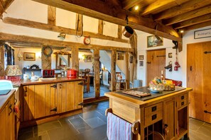A rustic kitchen with wooden beams, a wooden island with a sink, and various kitchen utensils hanging on the beams. - Premium Country Lodge With Hot Tub (Saint Asaph)